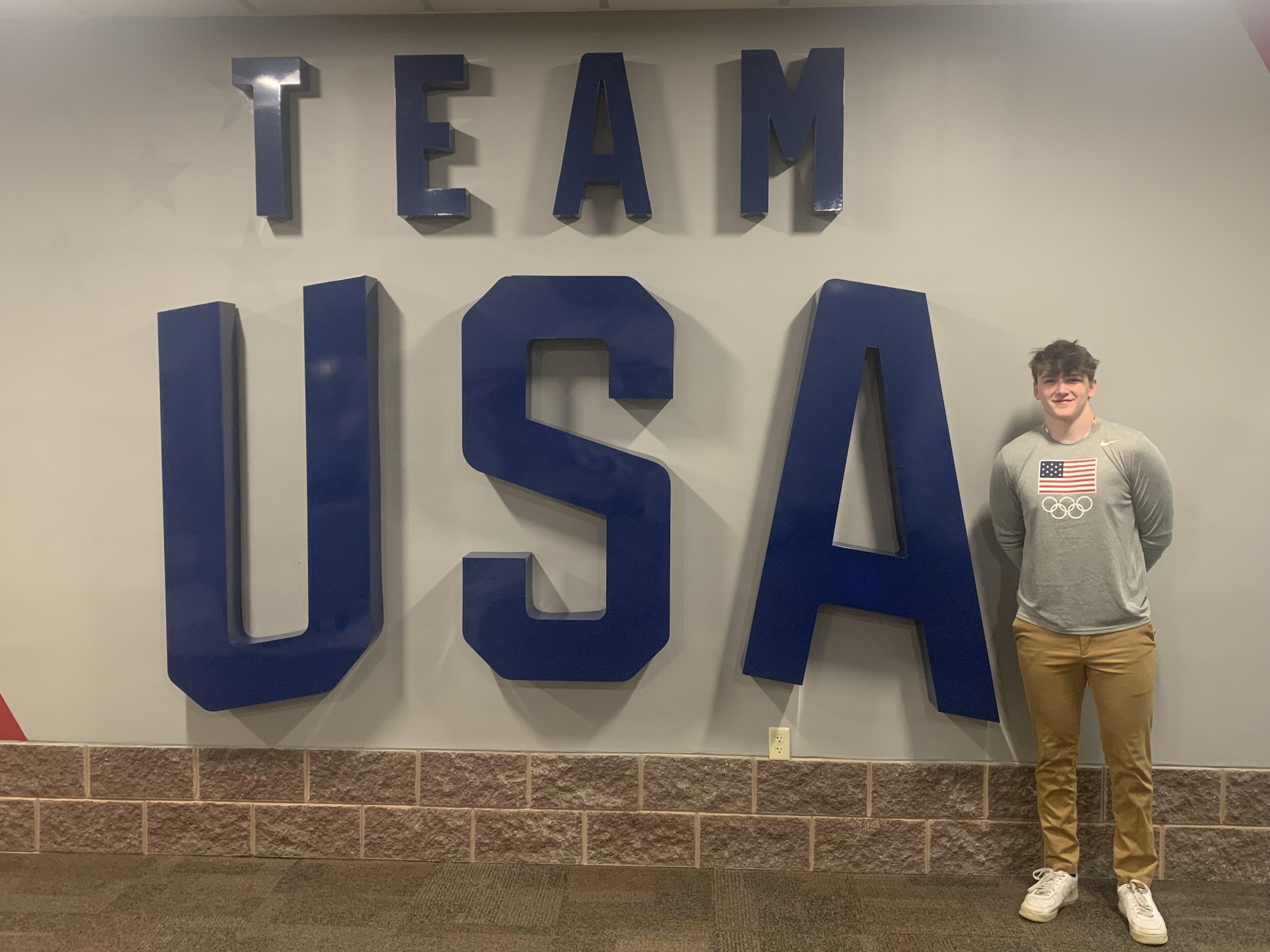 Logan standing proudly next to the Team USA wall at the Olympic Training Center